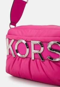 Borsa a tracolla imbottita rosa con un lucido logo argentato "KORS" su una larga tracolla. Caratterizzata da una chiusura con zip e una texture liscia.