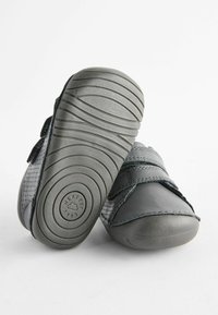 Chaussures pour tout-petits grises avec un dessus en cuir lisse, des côtés perforés et une semelle en caoutchouc flexible avec des motifs de bande en spirale et un logo.