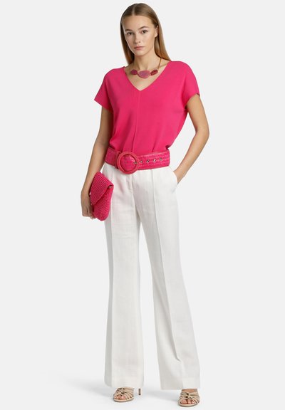 Fuchsia V-neck top, white wide-leg trousers, matching textured belt and clutch. Strappy beige sandals; layered necklace with pink accents.