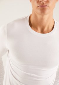 Witte shirt met lange mouwen, gemaakt van glad, rekbaar materiaal met een ronde halslijn. Getailleerd ontwerp met subtiele naaddetails.