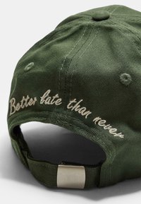 Cappellino verde scuro in cotone con visiera curva. Presenta un testo ricamato bianco che dice "Meglio tardi che mai" sul retro. Include una chiusura in metallo.