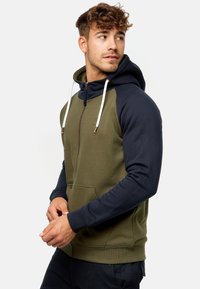 Sudadera con capucha que presenta un diseño en bloques de color caqui y azul marino, mangas largas, cierre con cremallera, bolsillo frontal y cordones de contraste.