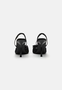 Sandalias de tacón alto negras con parte superior de tela texturizada, punta abierta y correa ajustable en el tobillo. Presenta un elegante tacón de aguja.