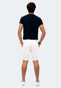 Navyblaues kurzärmeliges Hemd kombiniert mit weißen Shorts und weißen Sneakers. Die Shorts haben eine glatte Textur und eine klassische Passform, mit Gesäßtaschen.