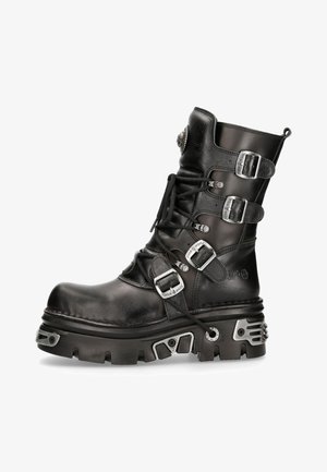 Botte de combat en cuir noir avec des détails de lacets et de boucles, semelle épaisse et accents en métal. Présente une forme arrondie et une finition texturée.