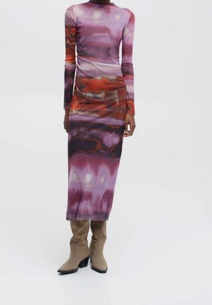 Femme portant une robe à manches longues et col montant avec des motifs abstraits violets et oranges, associée à des bottes beige à talons mi-mollet.