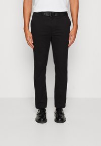 Schwarze Hosen mit schmaler Passform aus glattem Stoff, versehen mit einem Gürtel mit rundem Schnallenverschluss, kombiniert mit schwarzen Schuhen. Einfaches Design, ohne Muster.