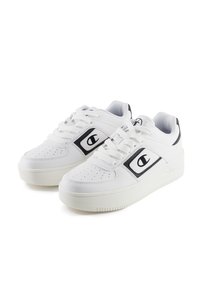 White sneakers with perforated toe box, contrasting black accents, and logo detail on the side. Thick white rubber sole for added height.