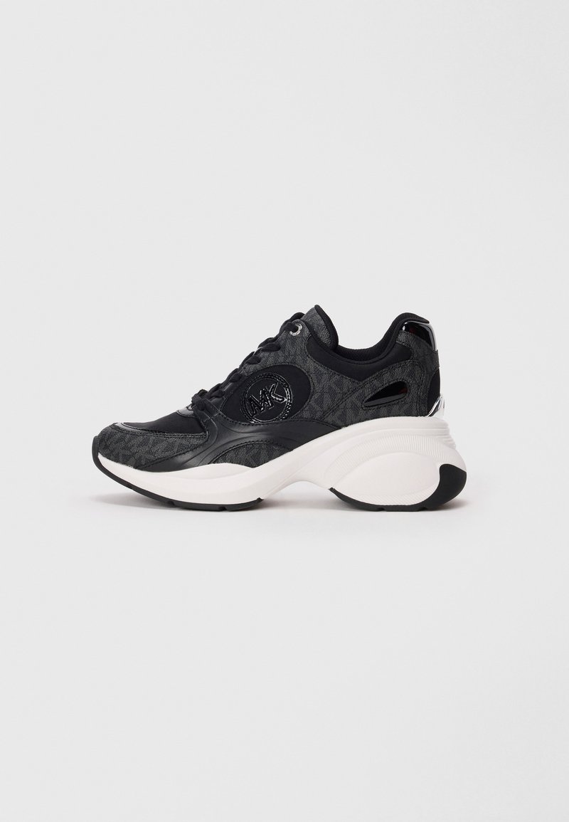 Sorte og grå Michael Kors sneakers med tykk hvit såle, snøring og logo på siden, mot en lys grå bakgrunn.