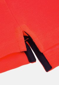 Czerwony, dziany materiał o teksturowanym wykończeniu, z bocznym rozcięciem podkreślonym granatowym wykończeniem. Gładka powierzchnia i widoczne detale starannego szycia.