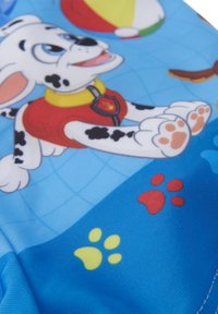 Tessuto blu con un cane dei cartoni animati con macchie nere, che indossa un gilet rosso. Lo sfondo include palloni da spiaggia colorati e motivi di impronte di zampe.