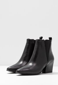 Schwarze Leder-Stiefeletten mit spitzem Zehenbereich, elastischen Seitenpaneelen und einem Blockabsatz in mittlerer Höhe, die eine glatte und glänzende Oberfläche aufweisen.