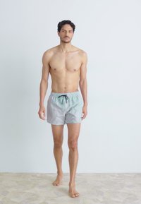 Calções de banho masculinos em azul claro com riscas horizontais. Apresentam uma cintura com cordão e são confeccionados em tecido leve.