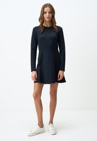 Robe bleue marine à manches longues avec un corsage ajusté et une jupe évasée, en tissu lisse, associée à des baskets blanches.