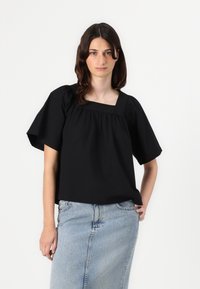 Top corto nero a maniche corte con scollo quadrato, dettagli arricciati e vestibilità comoda, abbinato a una gonna di jeans blu chiaro.