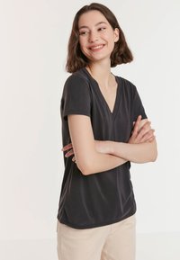 Zwarte V-hals T-shirt gemaakt van een gladde stof, met korte mouwen en een relaxte pasvorm, gecombineerd met lichtbeige broeken.