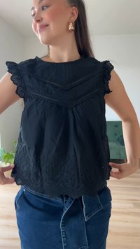 Črna bluza z čipkastimi detajli, valovitimi robovi in kapicami. Ima teksturirano tkanino in guban dizajn okoli pasu.