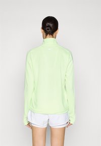 Light green zip-up jacket with long sleeves, high collar, and a small white logo on the back. Soft, smooth texture. Paired with white shorts.