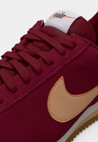 Κόκκινο σουέτ αθλητικό παπούτσι με υφή, με ταμπά δερμάτινο λογότυπο Swoosh, επενδυμένο γιακά και πλεκτά κορδόνια, τοποθετημένο σε λευκή σόλα.