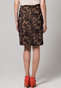 Pitkä pitsihame, jossa on musta kukkakuosi nude-vuorilla, takana halkio. Yhdistetty korallinvärisiin korkokenkiin.