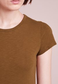 Oliwkowy t-shirt z krótkim rękawem o okrągłym dekolcie i miękkiej fakturze, charakteryzujący się dopasowanym krojem i minimalnymi detalami szwów.