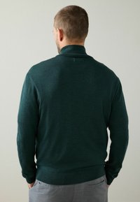 Mörkgrön pullovertröja med hög krage och ribbad fåll, gjord av mjukt stickat material. Enfärgad yta, inga synliga mönster eller detaljer.