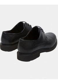 Chaussures en cuir noir avec une texture lisse, bout arrondi et design à lacets. Semelle épaisse noire avec un profil léger. La vue arrière montre des coutures minimales.