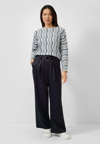 Lichtblauw-wit gestreept top met lange mouwen, gecombineerd met marineblauwe, wijde broek met hoge taille en witte sportschoenen. Voorzien van een ronde riemgesp.