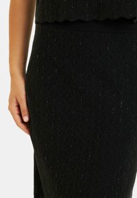 Czarna dzianinowa spódnica z fakturowanym wzorem diamentów i błyszczącymi akcentami. Dopasowana talia podkreśla sylwetkę. Zbliżenie.