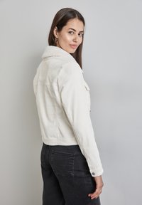 Vitt kordjacka med shearlingkrage, med knappdetaljer och en kort design. Matchas med svarta jeans.