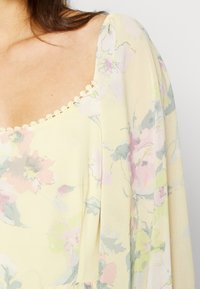 Blusa amarelo claro com um padrão floral em rosa e verde, apresentando um decote arredondado e um delicado acabamento em renda ao longo do decote.
