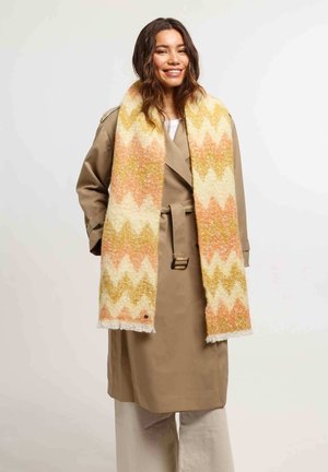 Barna trench coat fehér felső felett, egy puha sárga, narancssárga és krém színű, textúrált zig-zag mintás sál társaságában, francia végződésekkel.