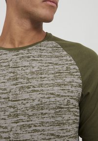 Grön och grå långärmad skjorta med ett strukturerat, randigt mönster på kroppen och enhetligt gröna ärmar, med rundad halsringning.