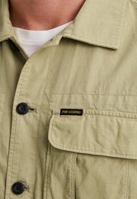 Light green corduroy jacket with a collar, black buttons, and a left chest pocket featuring a black and yellow PME Legend label.