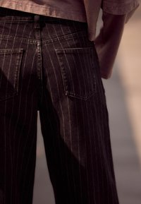 Mustad pinstripe'd teksad kõrge vöökohaga ja viie-tasku disainiga. Kanga tekstuur on denim, millel on peen sära ja kohandatud välimus.