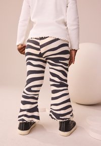 Stribede vide bukser i off-white og mørkegråt ribstof med en bølget kant, brugt sammen med sorte sneakers.