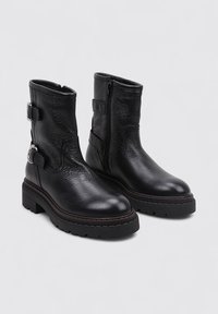 Bottines en cuir noir avec une finition texturée, des fermetures éclair sur le côté et des accents de boucle. Semelles en caoutchouc épaisses et un petit talon carré.