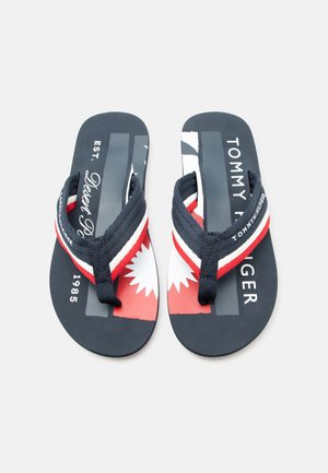Paar Tommy Hilfiger Flip-Flops in Marineblau, Rot und Weiß mit gebrandeten Riemen und grafischem Text auf den Fußbetten.