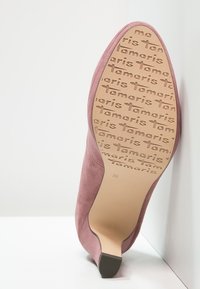 Ein einzelner mauvefarbener High-Heel-Schuh, aufrecht und schräg dargestellt, zeigt die Sohle mit dem "Tamaris"-Logo im Profil und der Größenmarkierung 39.