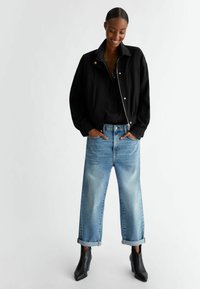Chaqueta corta negra, camisa negra, jeans anchos de tiro alto en azul desgastado remangados en el dobladillo, y botines negros con tacón. Diseño simple con un mínimo de detalles.