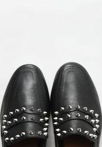 Mocassins en cuir noir ornés de clous métalliques argentés disposés en deux rangées horizontales sur le devant. Surface lisse avec un design à bout rond.