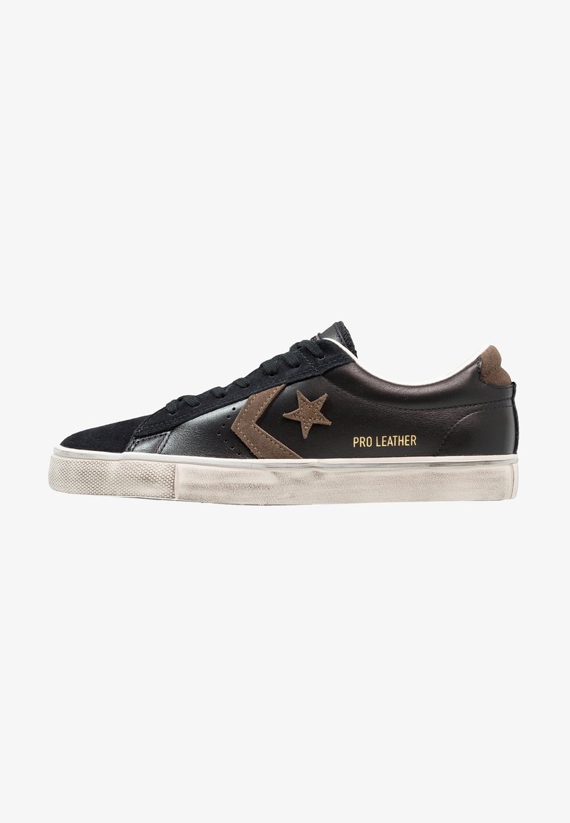 Black and brown leather sneaker with suede accents, rubber sole, star logo, and "PRO LEATHER" text in gold. Low-top design, lace-up closure.
