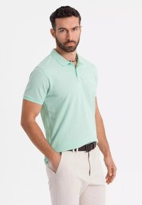 Polo shirt verde menta realizzato in tessuto morbido, con colletto, maniche corte e vestibilità slim, abbinato a pantaloni chiari.