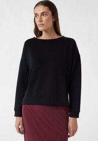 Zwarte sweatshirt van zacht materiaal met een wijde halslijn en lange mouwen, gecombineerd met een bordeauxrode rok. Glad textuur, relaxte pasvorm.