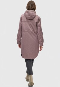 Long, pink, hooded coat with a textured fabric, drop-tail hem, and buttoned cuffs, paired with dark jeans and beige ankle boots.