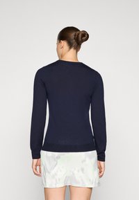 Mörkblå långärmad tröja med texturerad stickning, rundad halsringning och ribbad nederkant, bärs över en ljus mönstrad kjol.