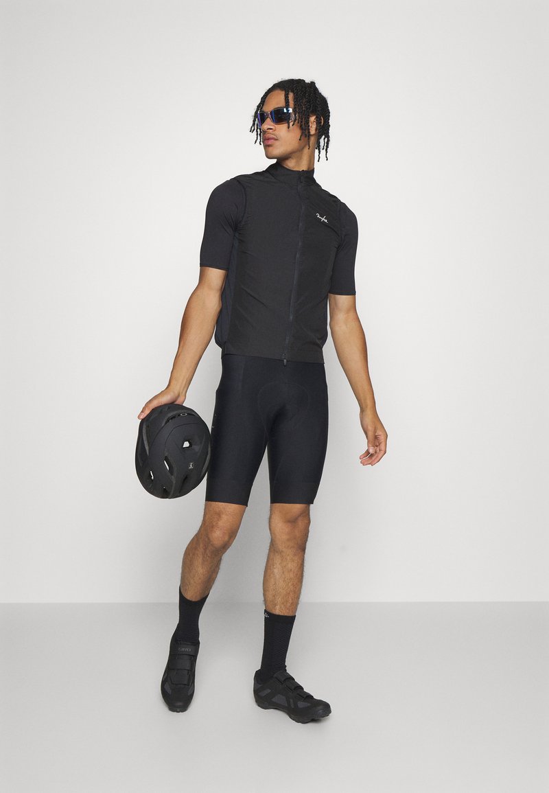 Maillot de cyclisme noir à manches courtes et fermeture éclair à l'avant, associé à un short rembourré noir. Les accessoires comprennent des chaussures de cyclisme noires et un casque.