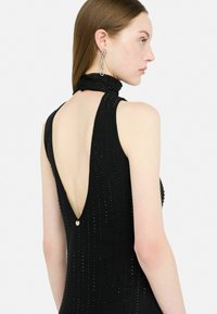 Abito nero senza schienale con collo alto, caratterizzato da dettagli in perline, un profondo scollo a V e una piccola accentatura in oro sul collo.