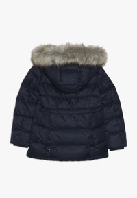 Námořnická modrá prošívaná bunda s kapucí lemovanou umělou kožešinou, horizontálním prošíváním a zapínáním na druky na spodním okraji a rukávech.