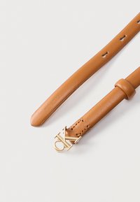 Παντελονάς δερμάτινη ζώνη σε αποχρώσεις της κανέλας με χρυσή αγκράφα «CK» και πολλαπλές τρύπες ρύθμισης σε λευκό φόντο.